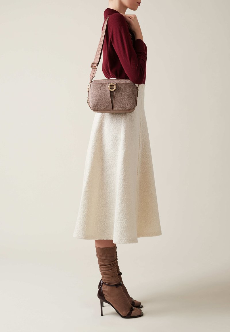 Donna che indossa un top bordeaux e una gonna midi in crema con texture, mentre porta una borsa a tracolla in taupe con una larga tracolla e una chiusura circolare.
