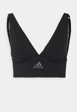 Soutien-gorge de sport noir avec un design en V profond, des bretelles ajustables et un logo Adidas gris imprimé à l'avant. Fabriqué à partir d'un tissu extensible.