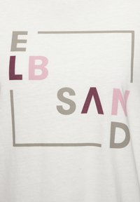 Weißes T-Shirt aus Stoff mit einem grafischen Design, das den Text "ELB SAND" in Grau, Rosa und Burgund in unterschiedlichen Größen und Stilen zeigt.