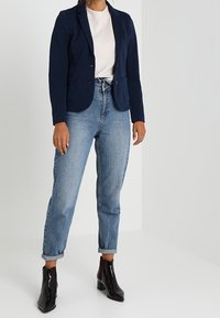Marinblå blazer med kledgeknäppa, två framfickor och en skräddarsydd passform, ihop med ljusblå jeans med uppvikt fåll och svarta ankelstövlar.