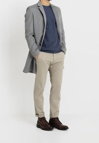 Grå ullkappa över en marinblå tröja, tan chinos och bruna snörskor. Fokusera på skräddarsydd passform och rena linjer, med en slät textur.