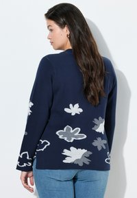 Granatowy sweter dzianinowy z białymi wzorami kwiatowymi, z okrągłym dekoltem, długimi rękawami i rozcięciem z boku na dole.