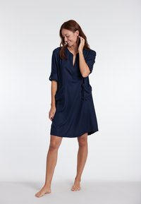 Abito blu navy con collo a camicia, maniche corte arrotolate e due tasche laterali; realizzato in un tessuto morbido e leggero.