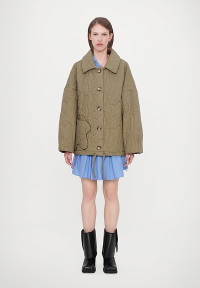 Quilted olive green jacket with oversized fit, large collar, wooden buttons, and front pocket. Paired with a blue pleated skirt and black boots.