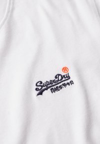 Hvid bomulds t-shirt med et marineblåt broderet "SuperDry" logo med en orange detalje. Blød tekstur, klassisk crew neckline.