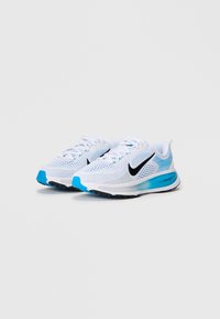 Sneakers atletici bianchi con tomaia in mesh, logo Nike nero, accenti blu sulla suola e sul tallone, design testurizzato per traspirabilità e supporto.