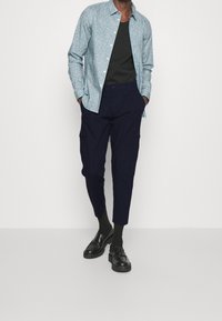 Ljusblå blommig knappupp skjorta över en svart linne, matchad med mörkblå cargobyxor och svarta loafers. Slät textur, skräddarsydd passform.