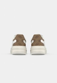 Paire de baskets blanches vues de dos, avec un tissu marron à motif présentant un logo répétitif sur la zone du talon.