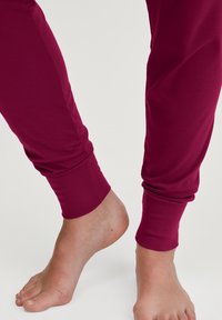 Bordeaux leggings met een aansluitend ontwerp, zachte stof en geribbelde boorden, gecombineerd met blote voeten op een neutrale achtergrond.