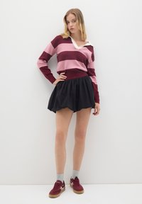 Bordeaux- und rosa gestreifter Pullover mit einem weißen Kragen, kombiniert mit einem schwarzen, puffigen Minirock und roten Sneakers mit weißem Akzent.