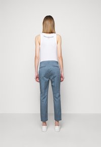 Camiseta sin mangas blanca con texto en la parte posterior, combinada con pantalones azul claro. Los pantalones tienen un diseño ajustado, piernas rectas y una textura suave.