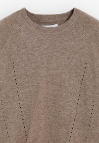 Bruine gebreide trui met een ronde hals en raglanmouwen, voorzien van kleine oogjes langs de zijkanten, zachte textuur.