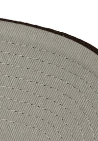 Tela circular gris con patrones concéntricos cosidos y un borde marrón oscuro. La textura parece suave y estrechamente tejida.