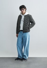 Siūtas tamsiai žalias švarkas su balta gaubtu, šviesiai mėlynos plačios kojinės džinsai ir juodi sportbačiai. Yra užtrauktukas ir šoninės kišenės.