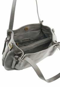 Sac à épaule en cuir gris avec bandoulière réglable, ouverture sur le dessus, poche intérieure zippée et fermeture à bouton magnétique.