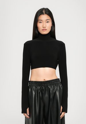 Maglione cropped nero a collo alto realizzato in tessuto morbido con maniche lunghe, abbinato a pantaloni in pelle nera a vita alta con cinturino elastico.