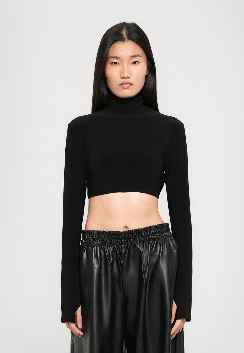 Melnā īsā turtlenecka krekls izgatavots no gludas auduma ar garām piedurknēm, apvienots ar augsto jostasvietu melniem ādas biksēm ar elastīgu jostasvītru.