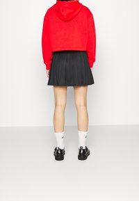 Kort röd hoodie med långa ärmar, tillsammans med en plisserad svart kjol. Vita ankelstrumpor och svarta skor fulländar looken.