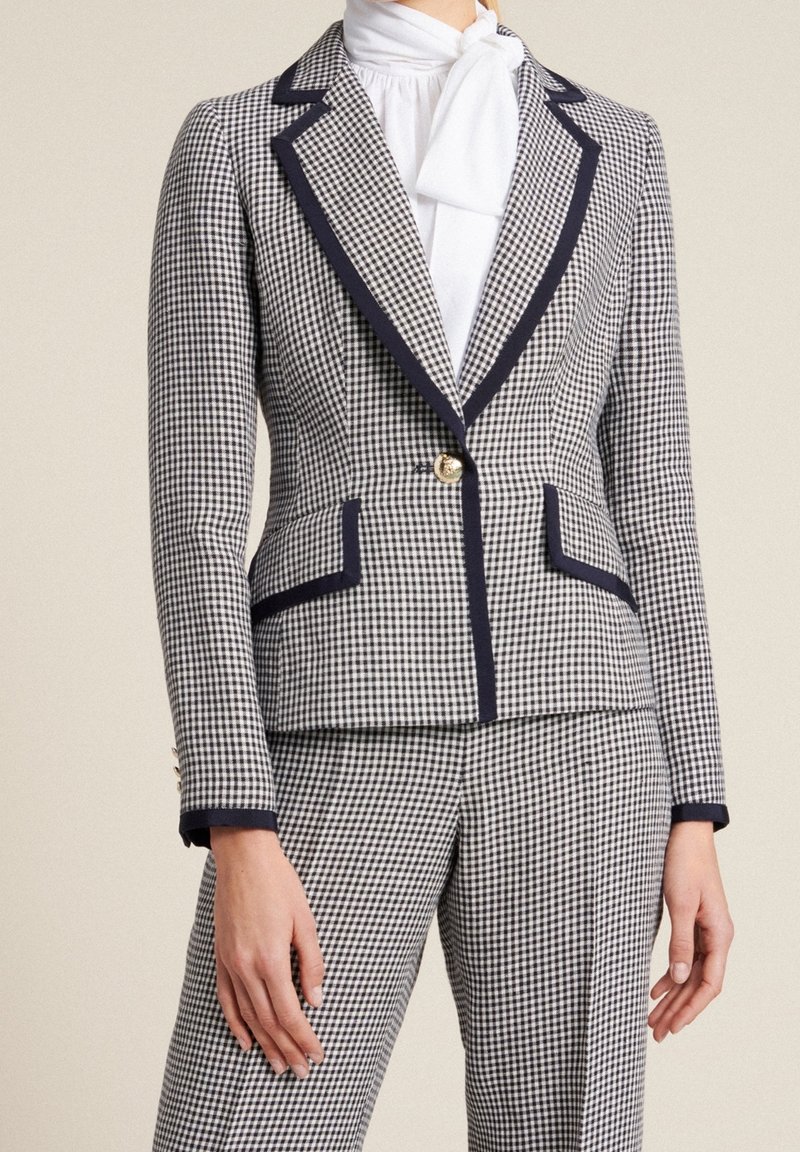 Dopasowana kraciasta marynarka w czerni i bieli, z granatowymi akcentami, złotym guzikiem, dwoma przednimi kieszeniami oraz ostrymi klapami.