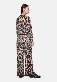 Leopardenmuster-Overall, leichtes Material, lange Ärmel, weit geschnittene Beine, schwarze Abschlüsse, mit auffälligen schwarzen und tanfarbenen Leopardenflecken.