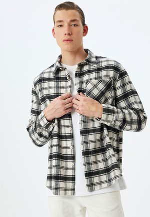 Sort-hvid ternet flannel skjorte med lange ærmer og knaplukning, der har en enkelt brystlomme og et blødt, struktureret stof.