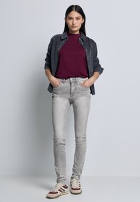 Camisa de pana gris sobre una camiseta burdeos, combinada con jeans skinny gris claro y zapatillas beige con acentos en burdeos, navy y crema.