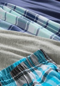 Collection de morceaux de tissu superposés. Comprend des nuances de gris uni, de bleu marine et des motifs à carreaux en bleu clair et noir, avec différentes textures et couleurs.