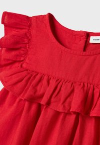 Robe en lin rouge avec un col rond, comportant une couche froncée le long des épaules et une silhouette ample et fluide. Étiquette visible.