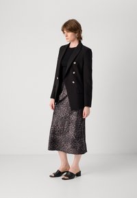 Svart dobbelspent blazer med gullknapper, parret med et skjørt i leopardmønster av satin og svarte sandaler med åpen tå og blokkheler.