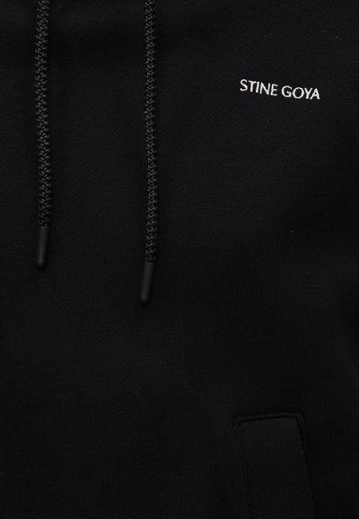 Μαύρο φούτερ με πλεγμένα κορδόνια και μικρό λευκό κεντημένο κείμενο "STINE GOYA" στο στήθος πάνω από την μπροστινή τσέπη.
