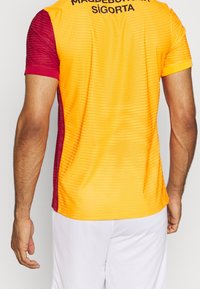 Camiseta deportiva de manga corta con un degradado que va del naranja al burdeos, tela texturizada y texto negro en la parte superior de la espalda.