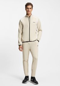 Beige track jacket and matching pants with black accents and zipper details. Features a high collar and "BOSS" logo on the chest and pants.