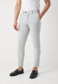 Světlé šedé kalhoty ve slim fit střihu, hladkého vzhledu, se zapínáním na jeden knoflík, kombinované s tmavými mokasíny pro kontrast.
