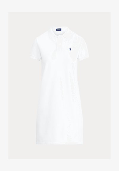 Hvit polokjole laget av bomull, med krage, korte ermer og et marineblått emblem på venstre bryst. Enkel design.