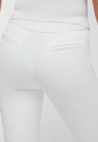 Pantaloni bianchi aderenti con tasche a filetto posteriori indossati con un top bianco abbinato, mostrando un primo piano della zona della vita e dei fianchi.