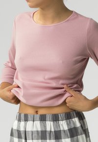 Jasnoróżowa, prążkowana bluzka z długim rękawem połączona z szaro-białymi, w kratkę spodniami od piżamy; tkanina wydaje się miękka i elastyczna, okrągły dekolt.