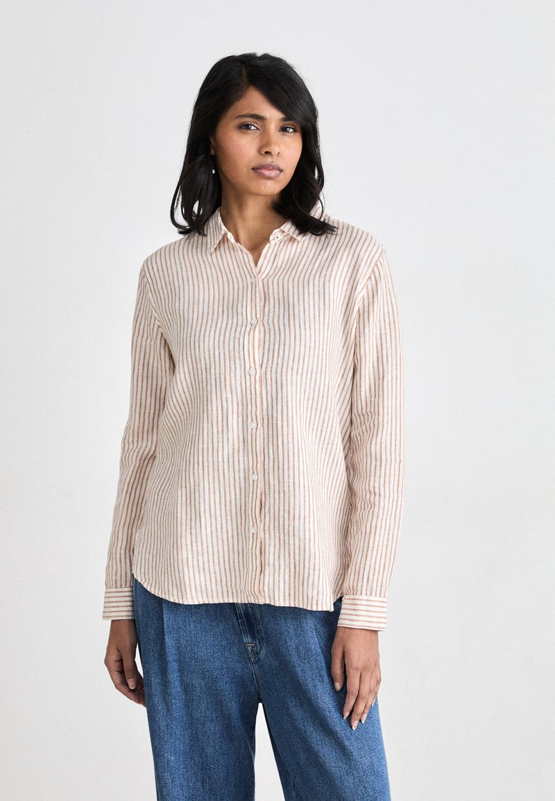 Long-sleeve button-up shirt in cream with peach vertical stripes. Features a collar and button closure, paired with loose blue denim pants.