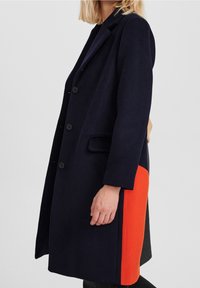 Abrigo de mezcla de lana en color azul marino con diseño de un solo botón, que cuenta con un panel lateral en un brillante color naranja, solapa con notch y dos bolsillos frontales.