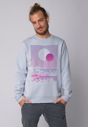 Lichtblauw sweatshirt met een grafisch ontwerp van horizontale strepen, cirkels in roze en grijs, en een bergsilhouet aan de onderkant.