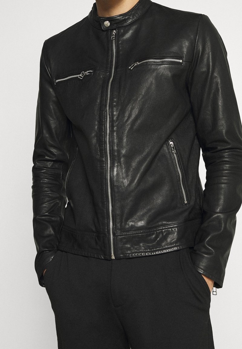 Černá kožená bunda s límcem do stoje, asymetrickými zipovými kapsami a přiléhavým střihem. Hladká textura s lesklým povrchem.