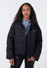 Schwarze Steppjacke mit Kapuze, Druckknöpfen und gestepptem Muster. Wird über einem hellblauen Hoodie getragen, der ein Logo auf der linken Brust hat.