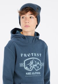 Felpa blu navy con una grafica che rappresenta occhiali da sci e paesaggio montano. Tessuto morbido, con una grande tasca frontale in stile kangaroo.