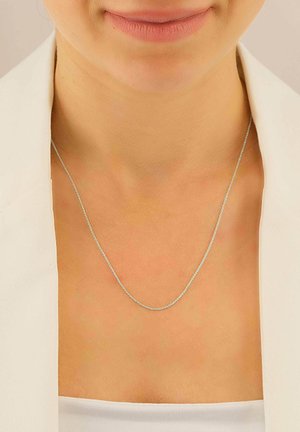 Collana d'argento con un fine design a catena attorcigliata. La catena poggia sulla clavicola, abbinata a una giacca bianca e a una maglietta semplice.