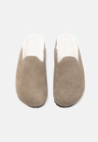 Grå mockaskor med en mjuk, vit fluffig foder, öppen baksidan och svarta gummisulor för bra grepp.