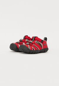 Czerwone buty wodne z czarną gumową podeszwą, otwarty design palców, regulowane paski i szare akcenty. Teksturowana cholewka zapewniająca oddychalność i elastyczność.