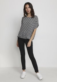 Svart och vit kortärmad topp med ett fläktmönster, ihopparad med svarta smala jeans och vita sneakers. Slät tyg, avslappnad passform.