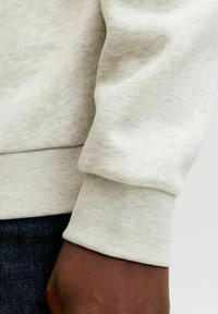Lichtgrijs sweatshirt met ribgebreide manchetten, gemaakt van zachte stof. De textuur lijkt glad met lichte variaties, terwijl de manchette strak en aangesloten is.