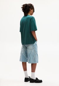 Tömör zöld oversized póló, tépett világoskék farmer bermuda short, fehér zokni és fekete fűzős cipő.
