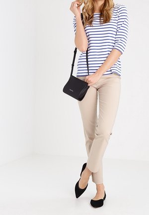 Black crossbody bag with a sleek design, adjustable strap, and subtle logo. Paired with a striped top and beige fitted pants.