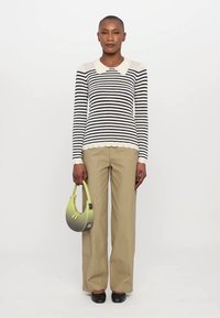 Maglione a righe bianco e nero con colletto bianco, abbinato a pantaloni beige a campana. Tiene una borsa a mezzaluna nei toni del verde e del grigio.